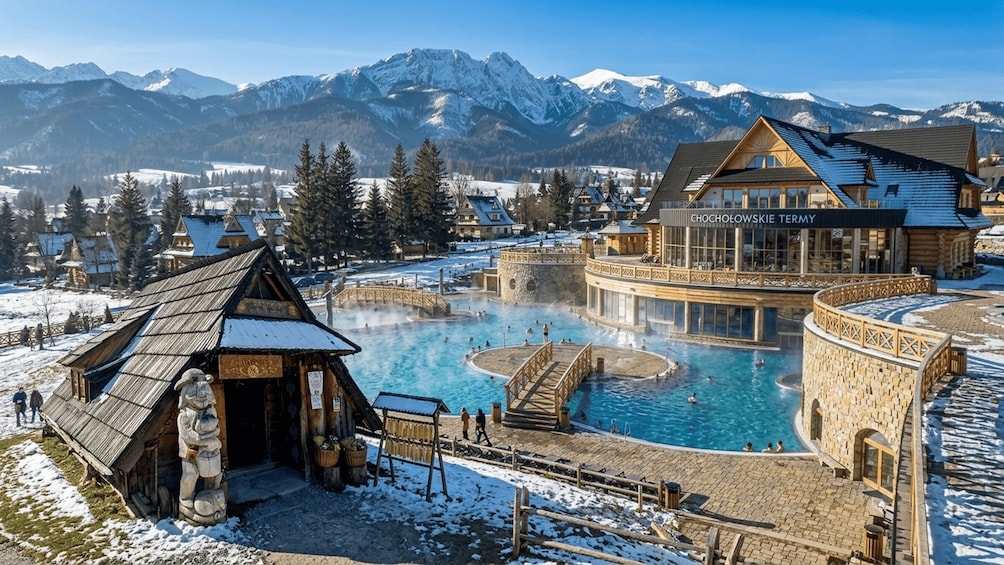 A hot spring resort with wooden cabins and a large pool surrounded by snow-covered mountains. 1