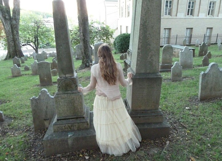 A woman in a white dress standing between gravestones in a cemetery. 4