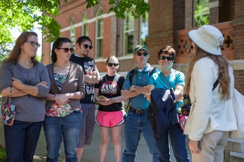 A group of people standing outdoors, some with bags, in front of a brick building with arched windows. 2