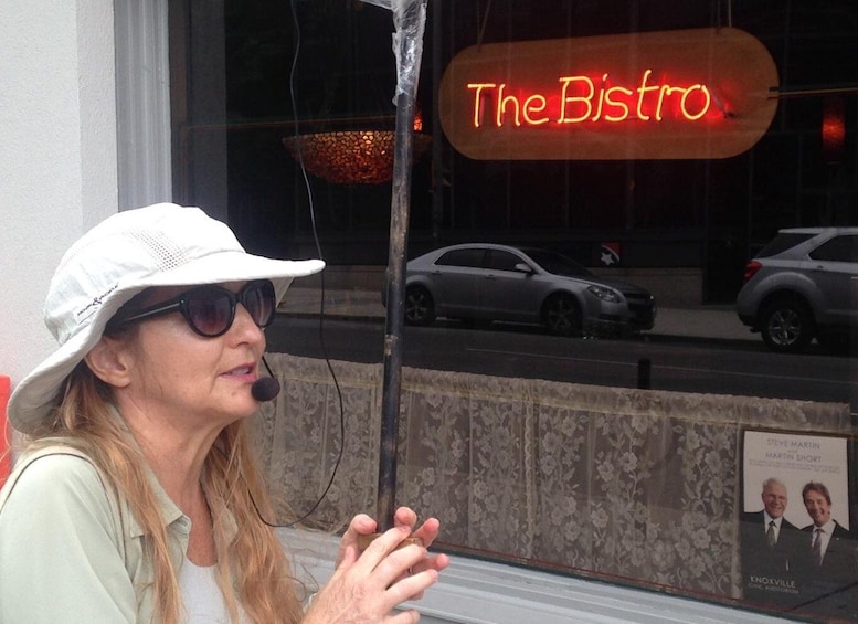 A person sitting by a window with a neon sign reading "The Bistro" in the background. 1