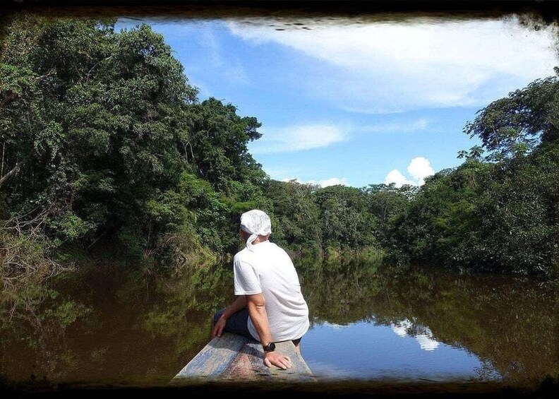 A person sitting on a rock by a calm river surrounded by dense greenery. 1