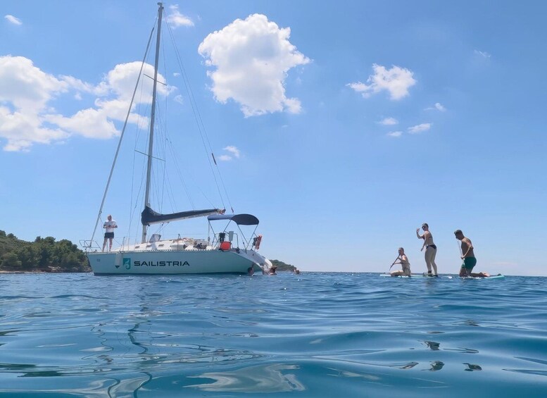 A sailboat named 'SAILISTRIA' on calm waters with people on the deck and some in the water. 1