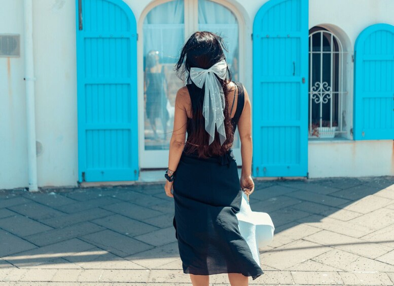 A person walking away from the camera on a paved street, with blue doors and windows in the background. 2