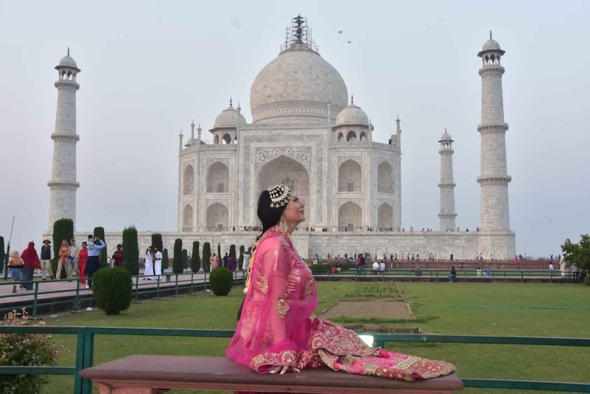 A person in traditional attire sitting on a bench with the Taj Mahal in the background. 5