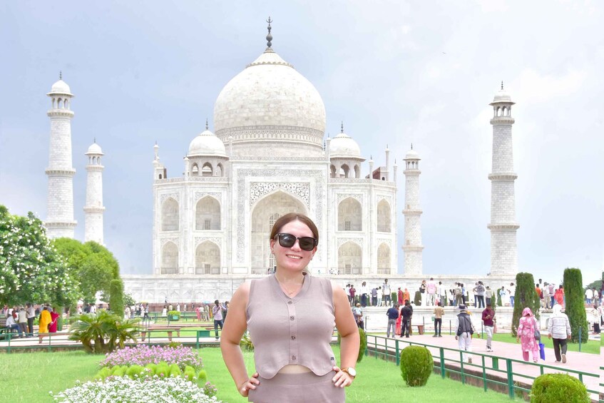 A person standing in front of the Taj Mahal with its four minarets and a garden with pink flowers. 1