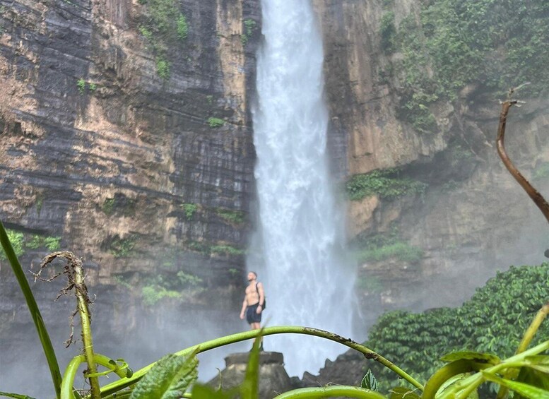 A waterfall cascading down a rocky cliff with a person standing at the base. 2