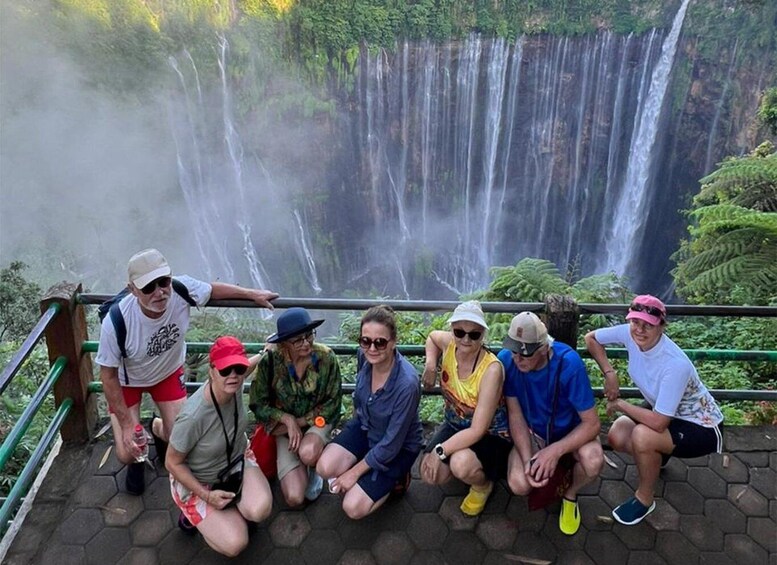 A group of people posing in front of a waterfall with lush greenery in the background. 5