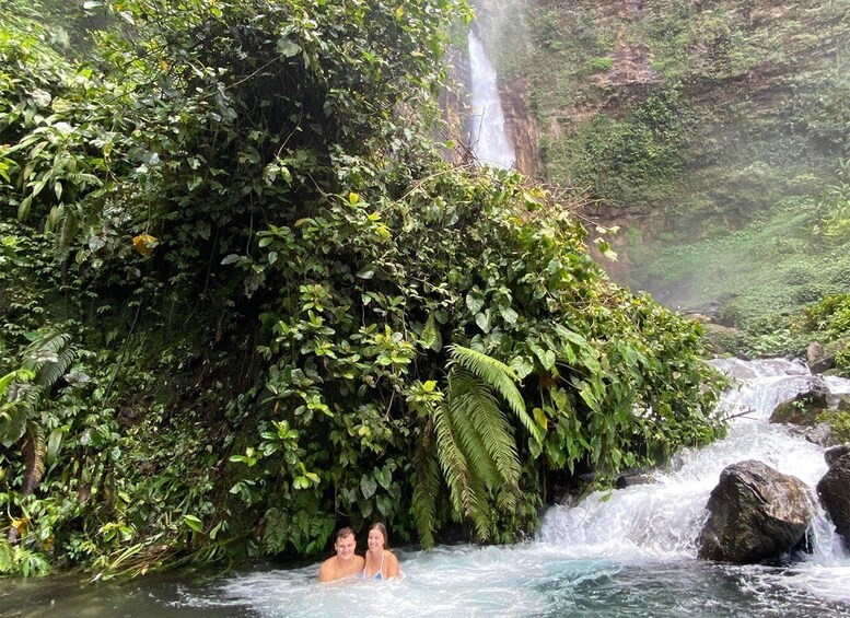 A waterfall, dense greenery, and a couple in a natural hot spring. 4