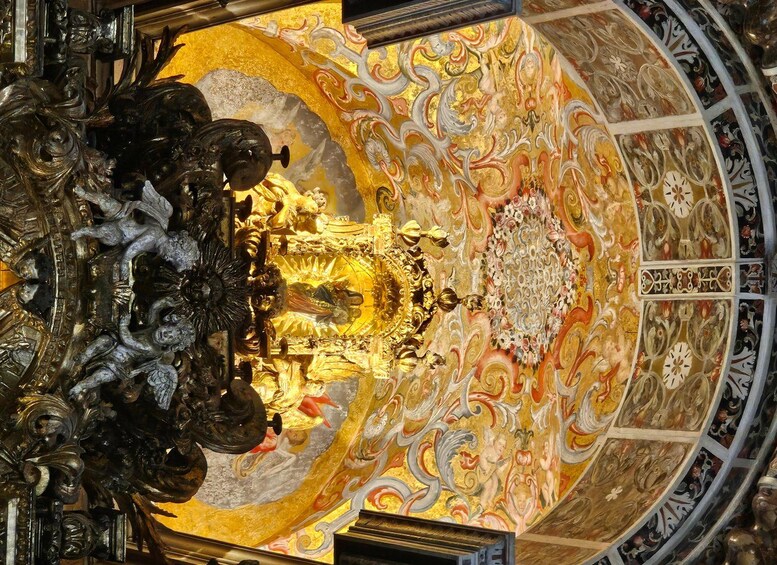 A detailed ceiling with ornate gold and white patterns, a central chandelier, and a circular design. 2