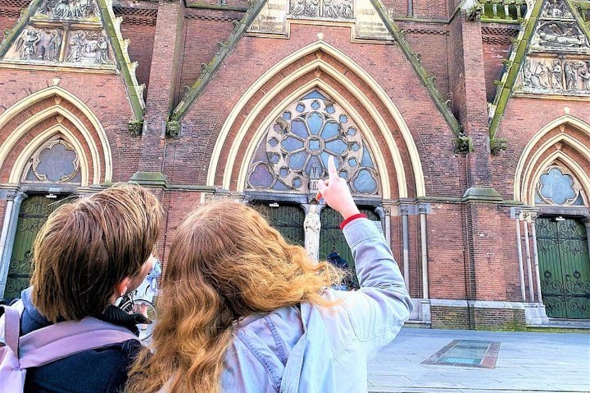 Deux personnes se tiennent face à un bâtiment historique, caractérisé par ses arcs en ogive et ses sculptures en pierre détaillées. 4