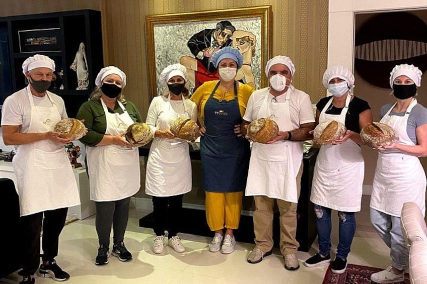 Un grupo de personas sosteniendo hogazas de pan en una habitación con un cuadro al fondo. 1