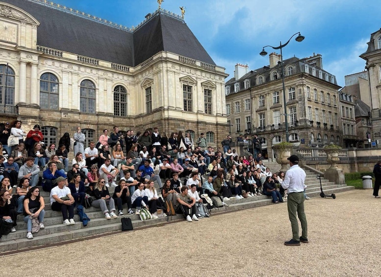 A large crowd seated on steps in front of a historic building with classical architecture. 3