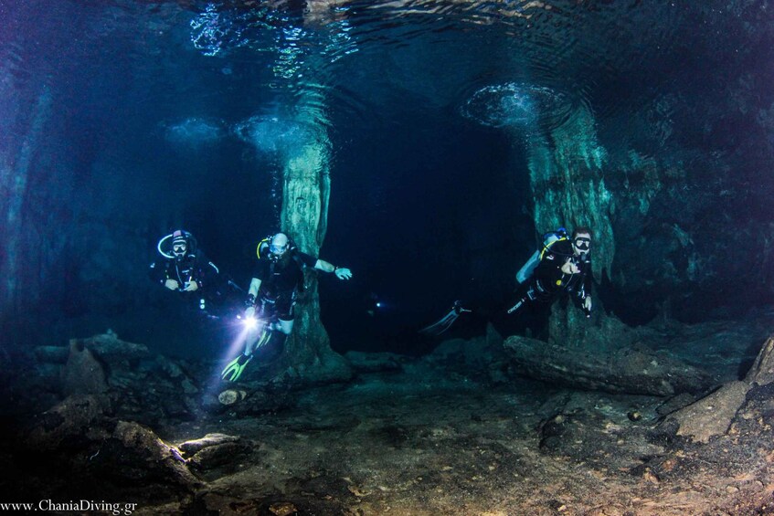 Divers exploring an underwater cave with rocky formations and a narrow passage. 4