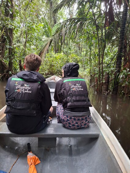 Two people in a boat surrounded by dense tropical vegetation. 1