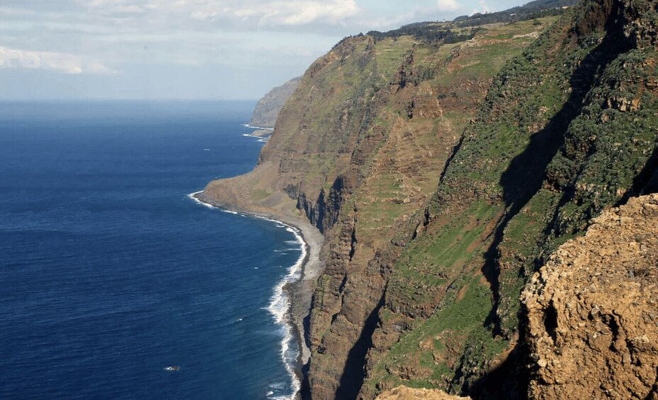 A coastal cliff with a narrow beach and deep blue ocean. 2