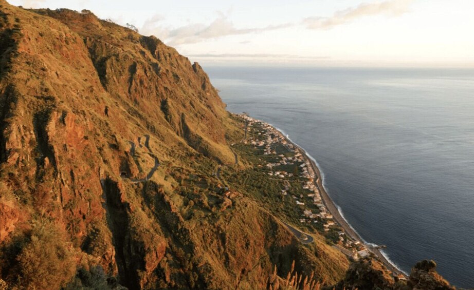 A coastal landscape with a steep cliff and a winding road leading to a beach. 5