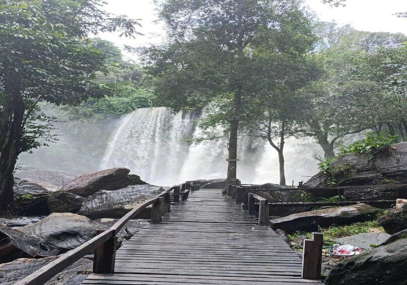 A wooden boardwalk leading to a waterfall surrounded by trees. 2