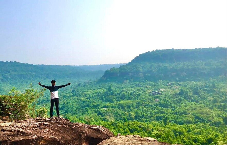 A person standing on a rock with arms outstretched, overlooking a lush green valley. 4