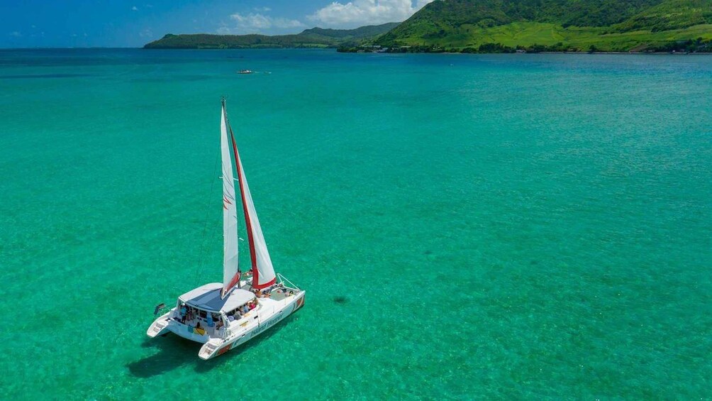 A sailboat on turquoise waters with a green hillside in the background. 3