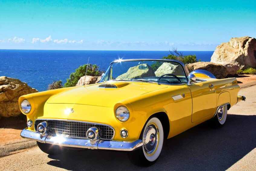 A yellow vintage convertible car parked on a coastal road with a clear view of the ocean and rocky cliffs in the background. 5