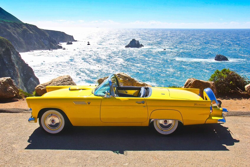 A yellow convertible car parked on a coastal road with a view of the ocean and rocky cliffs. 1