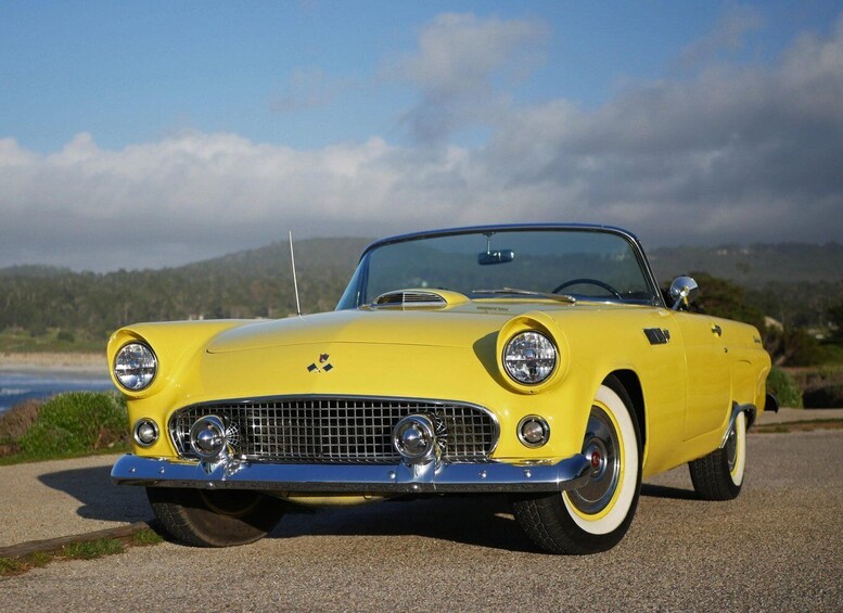 A yellow convertible car parked on a coastal road with a scenic view of the ocean and hills in the background. 3