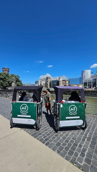Two green electric rickshaws parked on a cobblestone path with a historic building in the background. 2