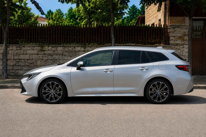 A silver car parked on a street with a stone wall and a wooden fence in the background. 2