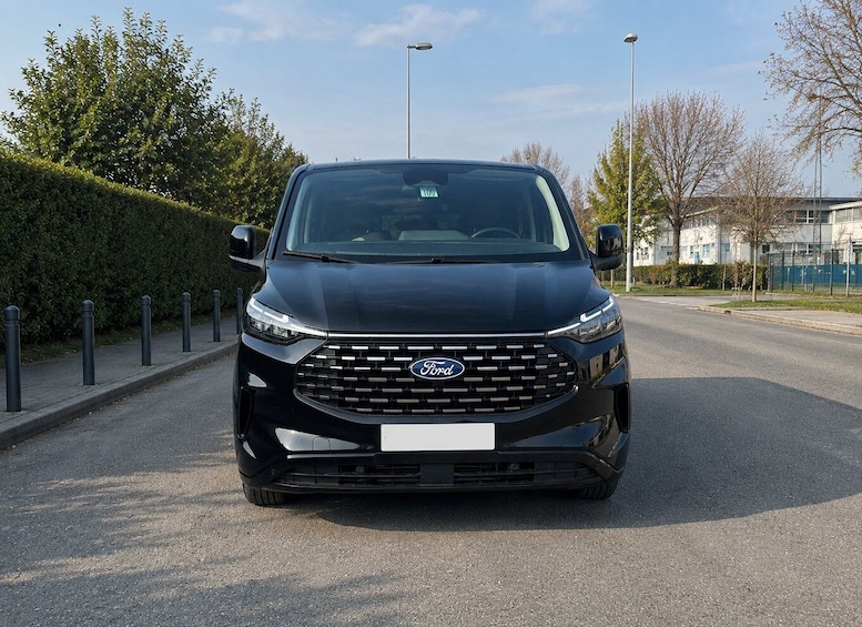 A black Ford van parked on a road with a hedge and buildings in the background. 1