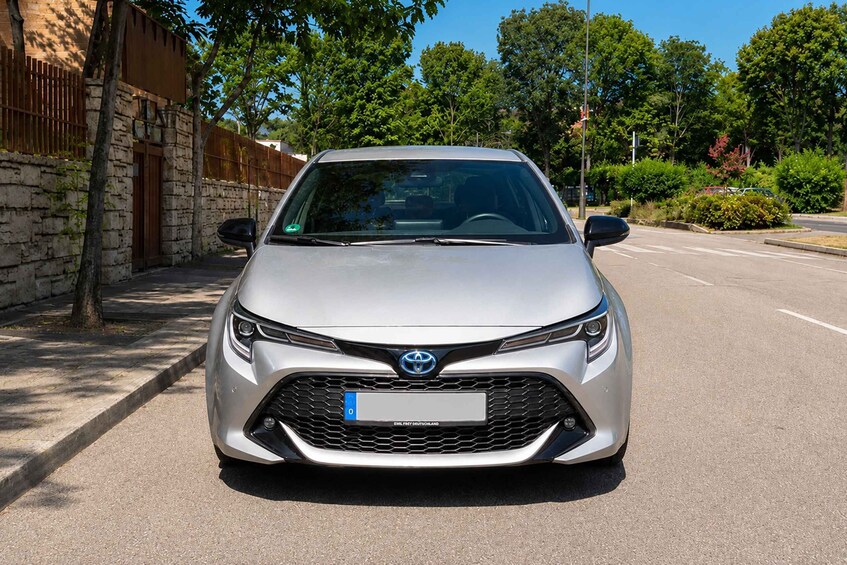 A silver Toyota parked on a street with a stone wall and trees in the background. 4