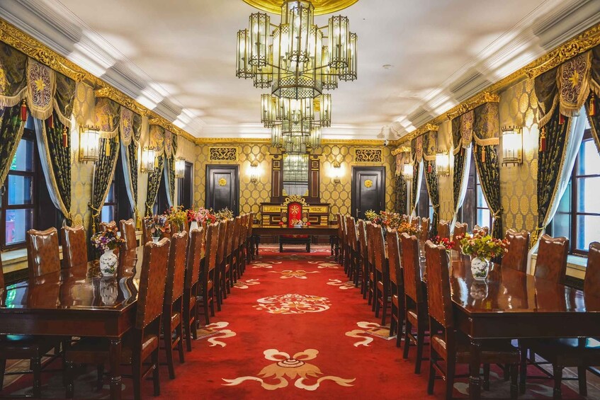 A grand hall with ornate chandeliers, a red carpet, and rows of wooden chairs. 3
