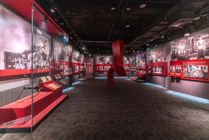An indoor exhibition space with red and black displays, featuring historical photographs and information panels. 2