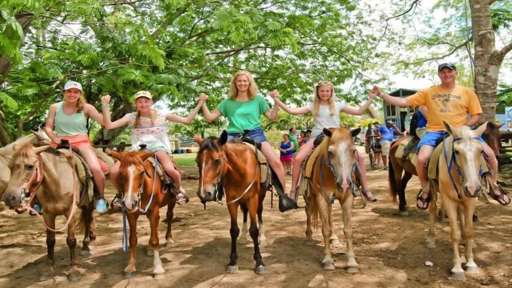 People riding horses in a line on a dirt path surrounded by trees. 2
