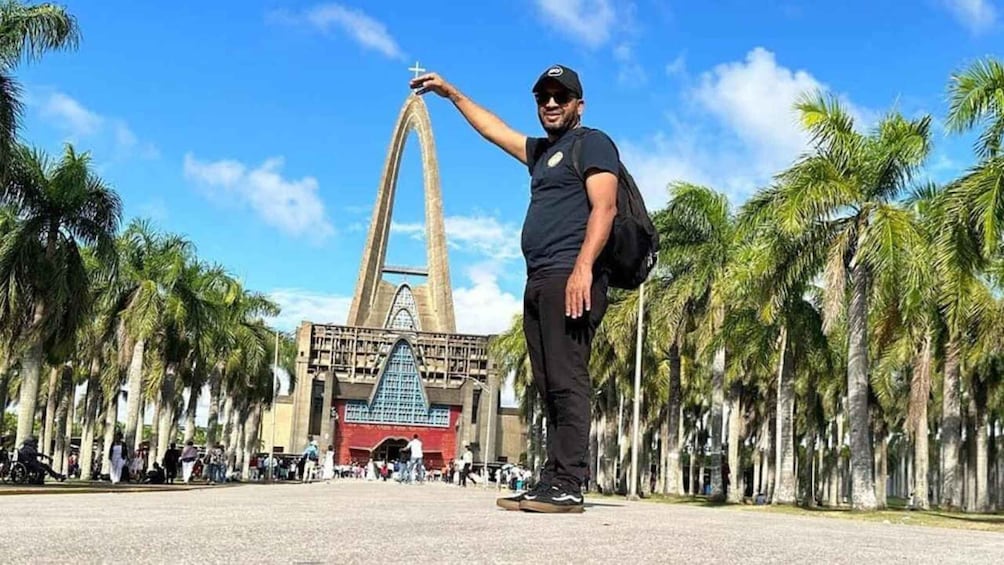 A person standing in front of a large building with a triangular entrance, surrounded by palm trees. 4