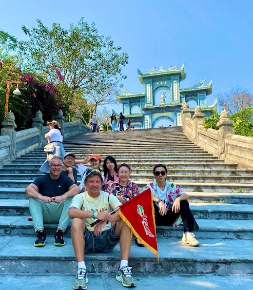 A group of people sitting on stone steps in front of a traditional building with a blue roof and golden decorations. 4