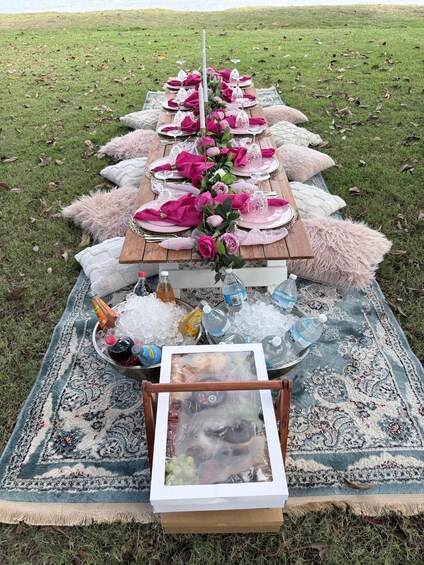 A picnic setup with a long table, pink napkins, and a bottle of water. 3
