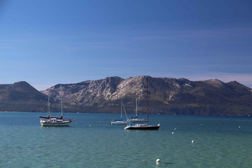 A calm lake with several sailboats anchored near the shore, surrounded by mountains. 3