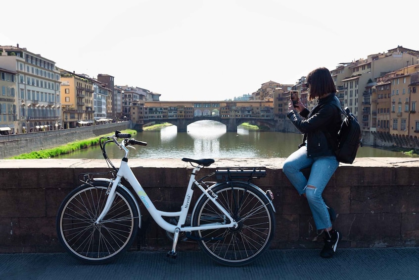 A white bicycle parked by a canal with a bridge in the background. 1