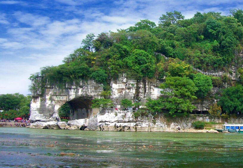 Une grande formation rocheuse dotée d’une entrée de tunnel, entourée d’une végétation luxuriante et bordée par une rivière. 4