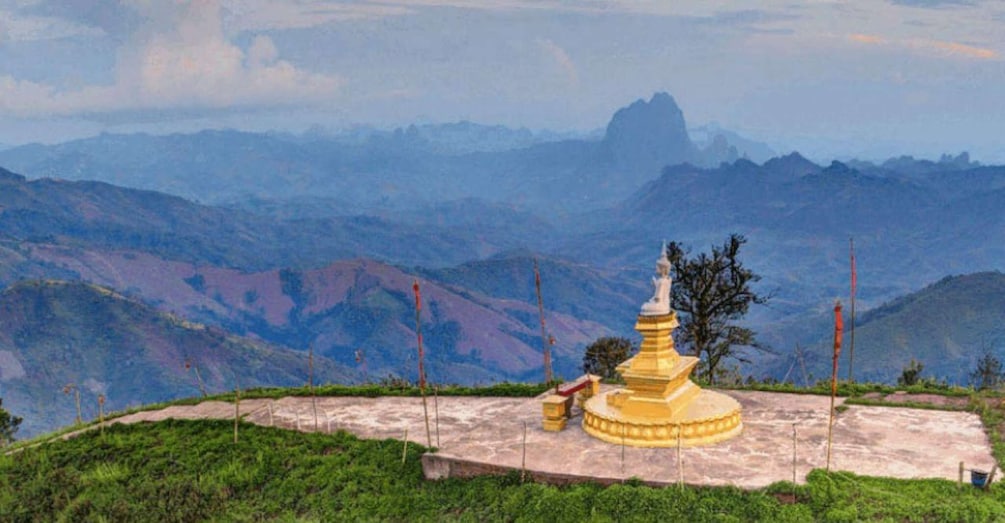 A golden stupa on a hilltop with a mountain range in the background. 3
