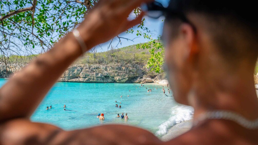 Een strand met helder turquoise water en mensen die zwemmen en zonnebaden. 3