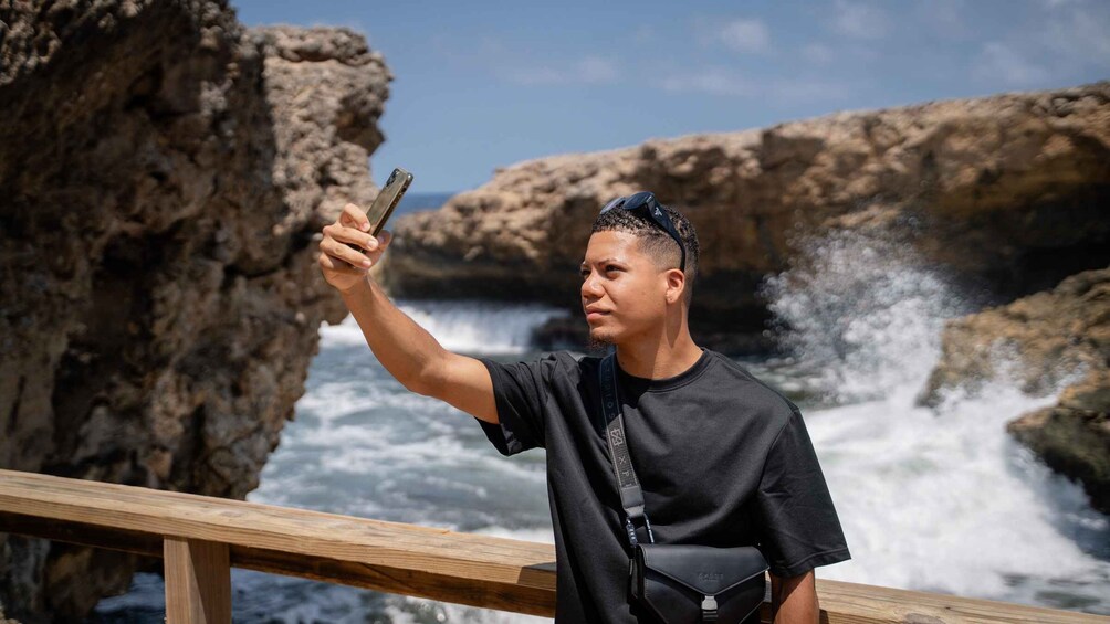 Iemand maakt een selfie met een smartphone bij een rotsachtige kustlijn waar golven breken. 2