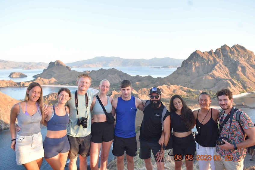 A group of people standing on a cliff overlooking a coastal landscape with mountains and a body of water in the background. 5