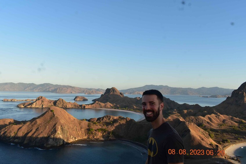 A person standing on a rocky outcrop overlooking a coastal landscape with hills and a beach. 3