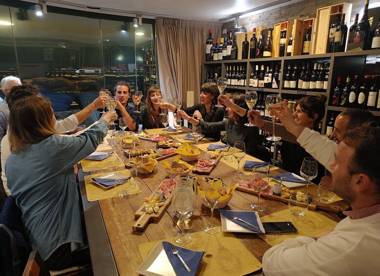 A group of people toasting at a table with wine glasses, surrounded by a wine rack with various bottles. 1