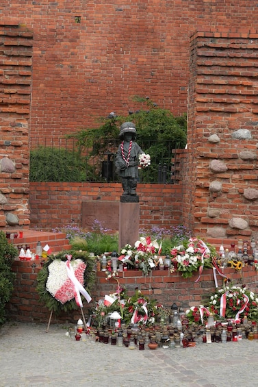A statue with a wreath and flowers, surrounded by memorials and offerings. 2
