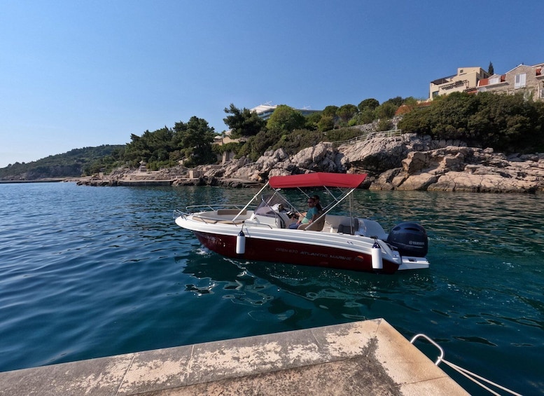 A boat named "Open 670 Atlantic Marine" docked at a pier with a rocky coastline and buildings in the background. 3