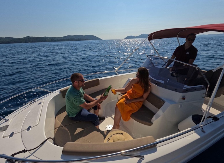 A boat with two people sitting and one person standing, on a calm sea with distant land. 2