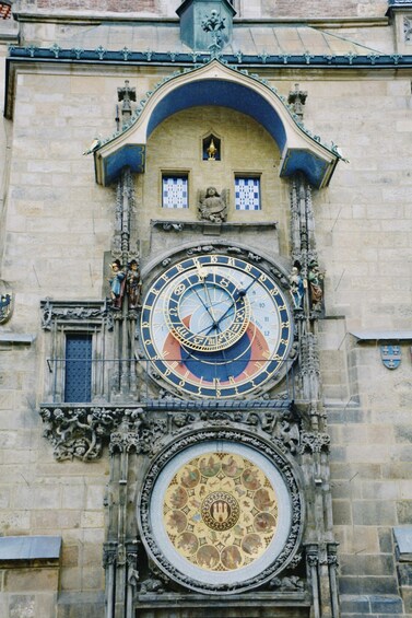 A historic building with a large, ornate clock featuring a zodiac design, surrounded by intricate stone carvings and a smaller clock below. 3