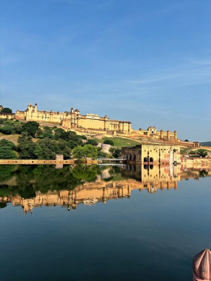 A historic fort with a reflection in the water, surrounded by greenery and a clear sky. 3